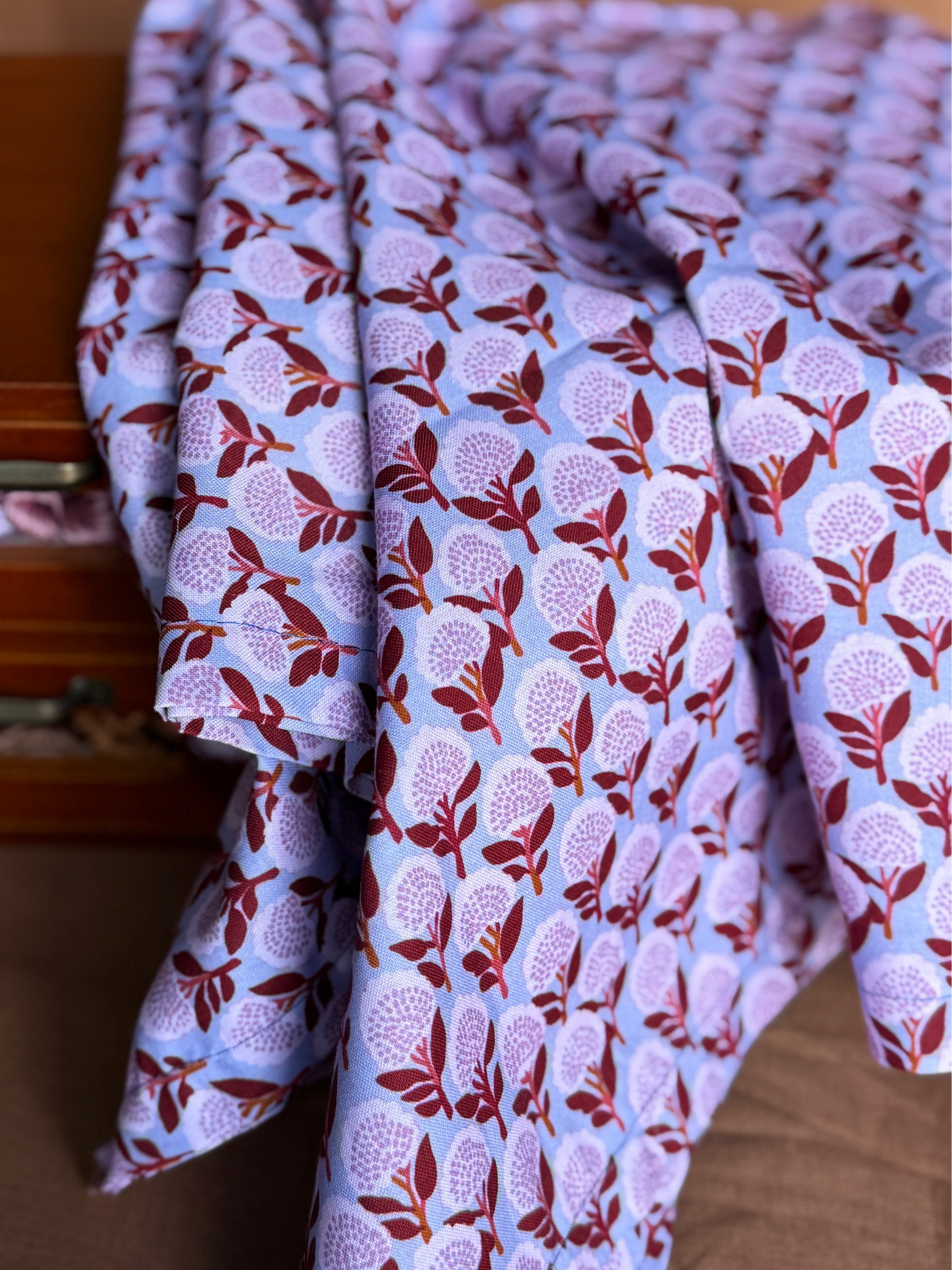 Folded fabric with a floral pattern in front of a wooden drawer.