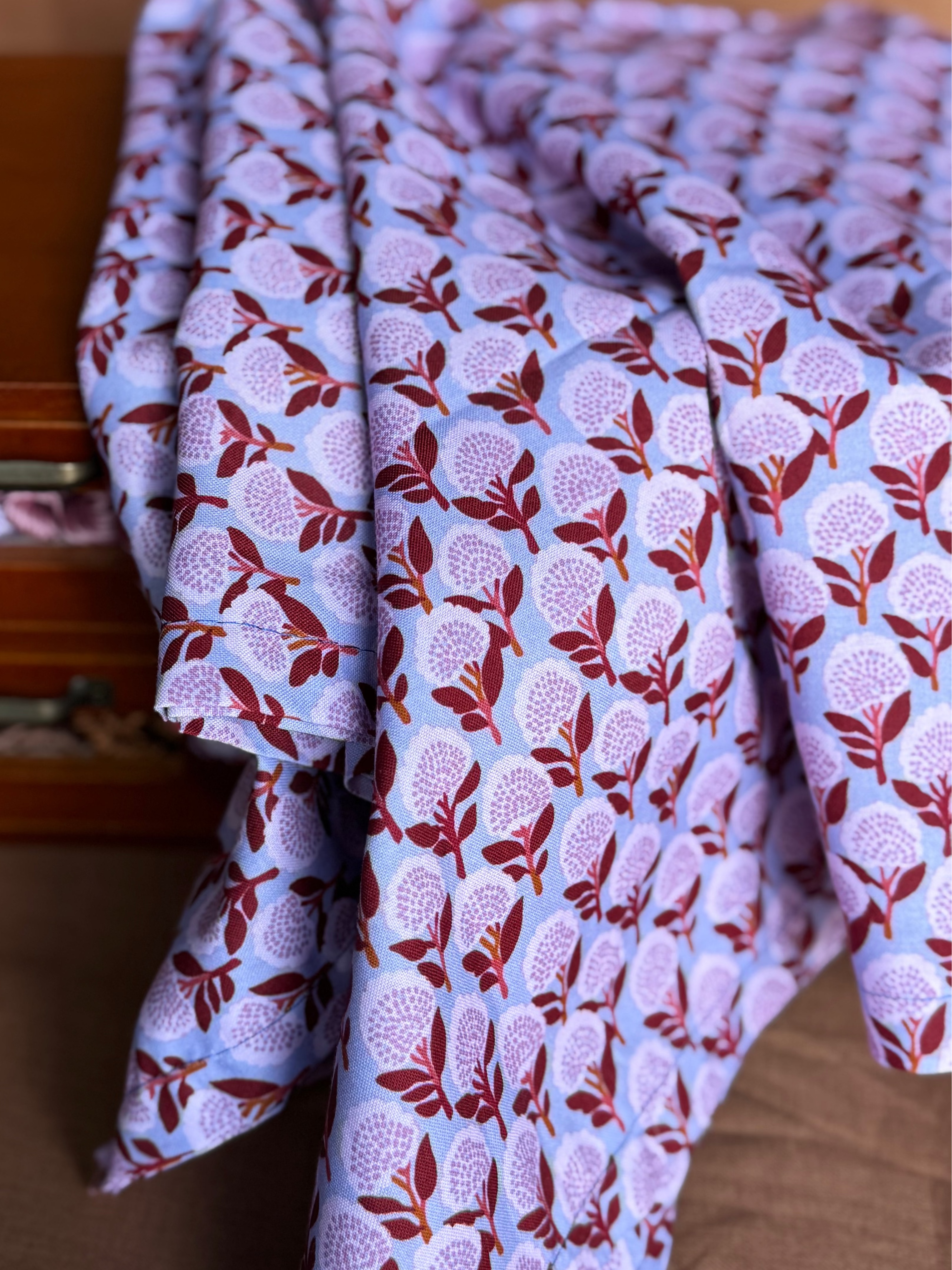 Folded fabric with a floral pattern in front of a wooden drawer.